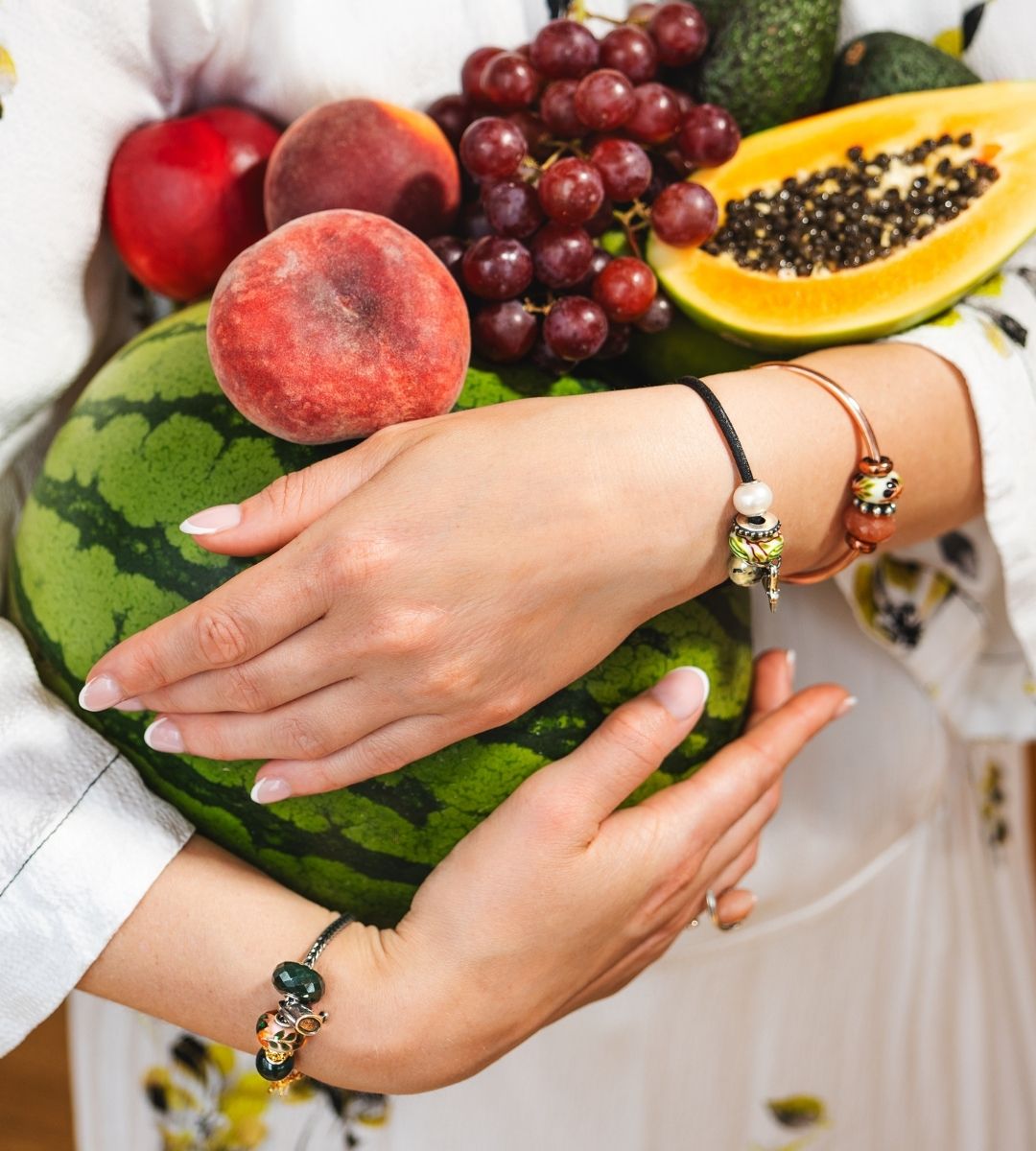 Model holding various fruit while wearing bracelets with different beads